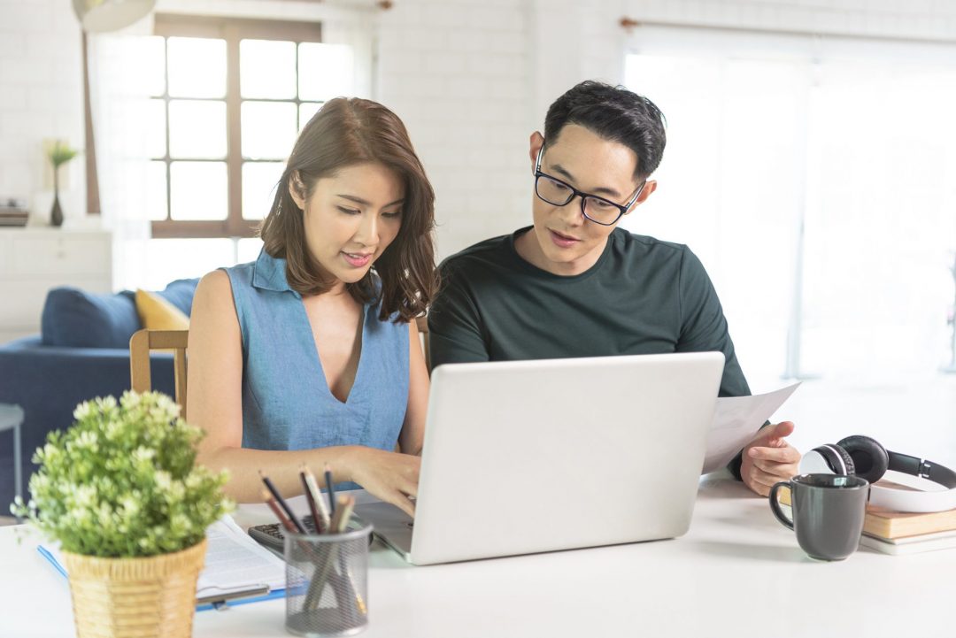 serious Asian husband checking analyzing statement utilities bills sitting together at home.